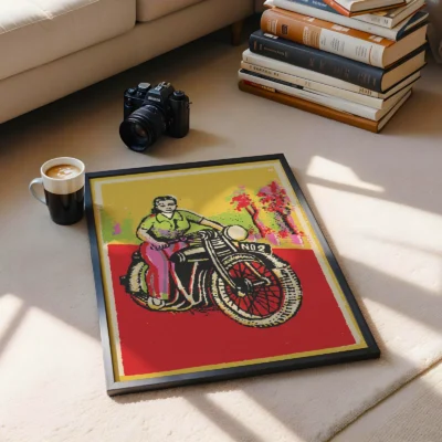 A framed art print of a woman on a motorcycle with a colorful background, placed on a floor next to a coffee cup and a camera.