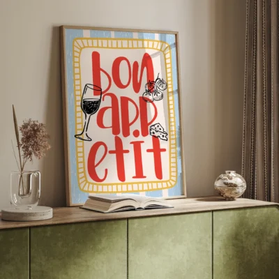 A framed wall art displaying the phrase 'Bon Appétit' with illustrations of wine, cake, and cheese