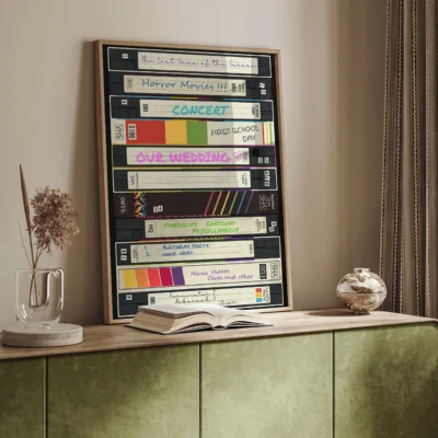 Framed artwork of VCR tapes with labels for personal memories, sitting on a green console table