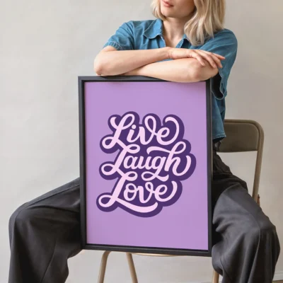 Person holding purple framed “Live Laugh Love” quote poster with retro design.