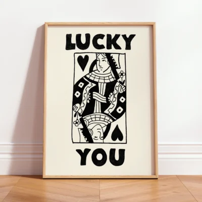 Black and cream Queen of Hearts poster in black frame, styled on shelf with plants in modern interior.