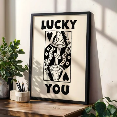 Black and cream Queen of Hearts poster in black frame, styled on shelf with plants in modern interior.