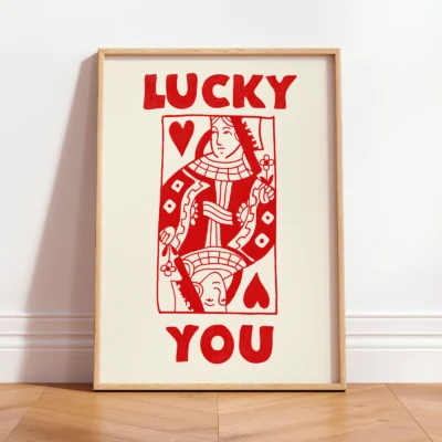 Framed red and cream Queen of Hearts poster leaning against wall, hand-drawn retro playing card style.