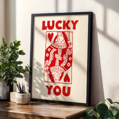 Red and cream Queen of Hearts poster in black frame, styled on shelf with plants in modern interior.