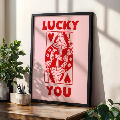 Red and pink Queen of Hearts poster in black frame, styled on shelf with plants in modern interior.