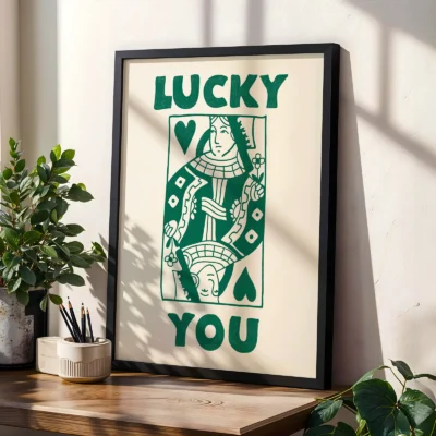 Green and cream Queen card poster in black frame, styled on shelf with plants in a modern interior.