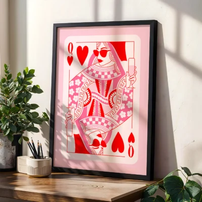Pink and red Queen of Hearts poster in black frame, styled on shelf with plants in modern interior.