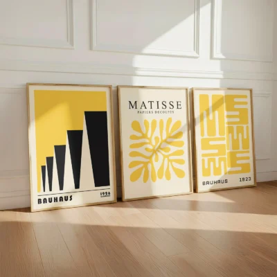 Trio of yellow Bauhaus posters resting on wooden floor against white wall