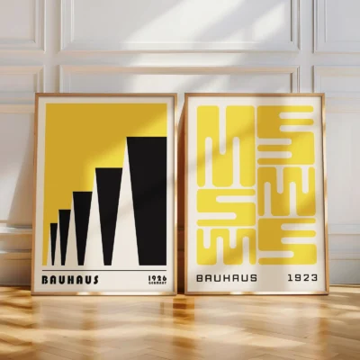 Two Bauhaus posters leaning against a bright white wall on a wooden floor.
