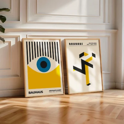 Framed Bauhaus posters resting on the floor in a bright white-paneled room.